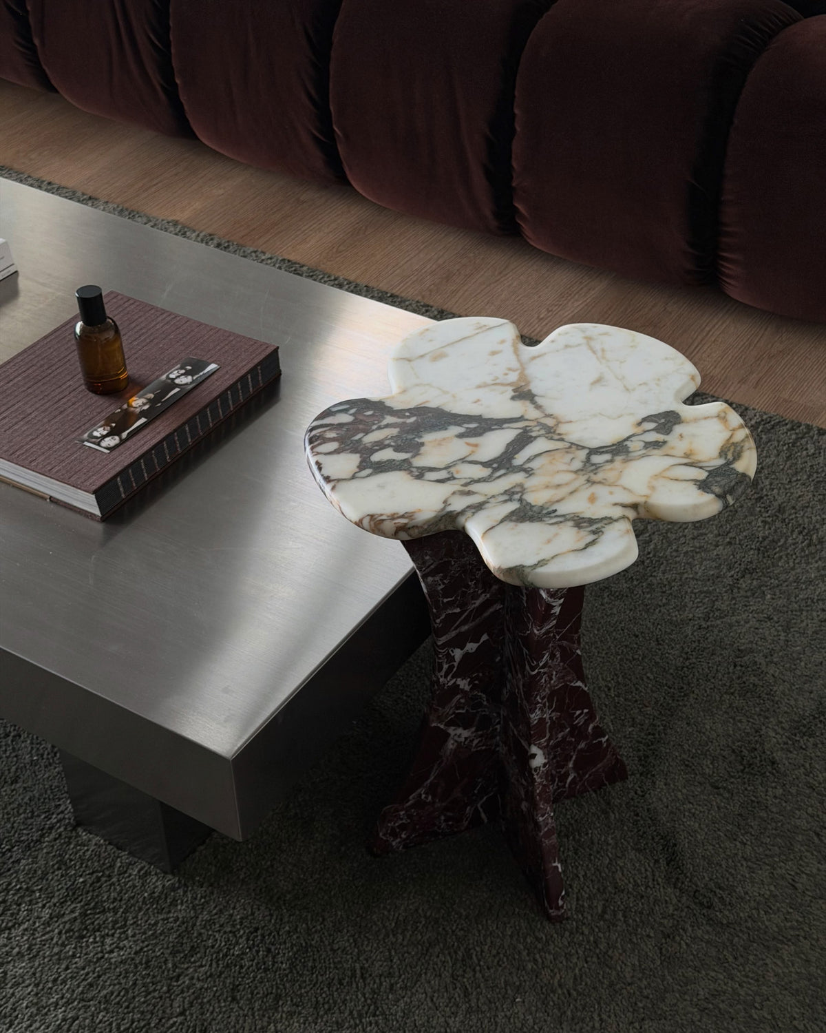 A sculptural flower-shaped marble side table next to a stainless steel coffee table.