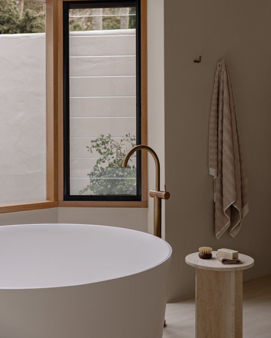 Small travertine side table styled in a bathroom