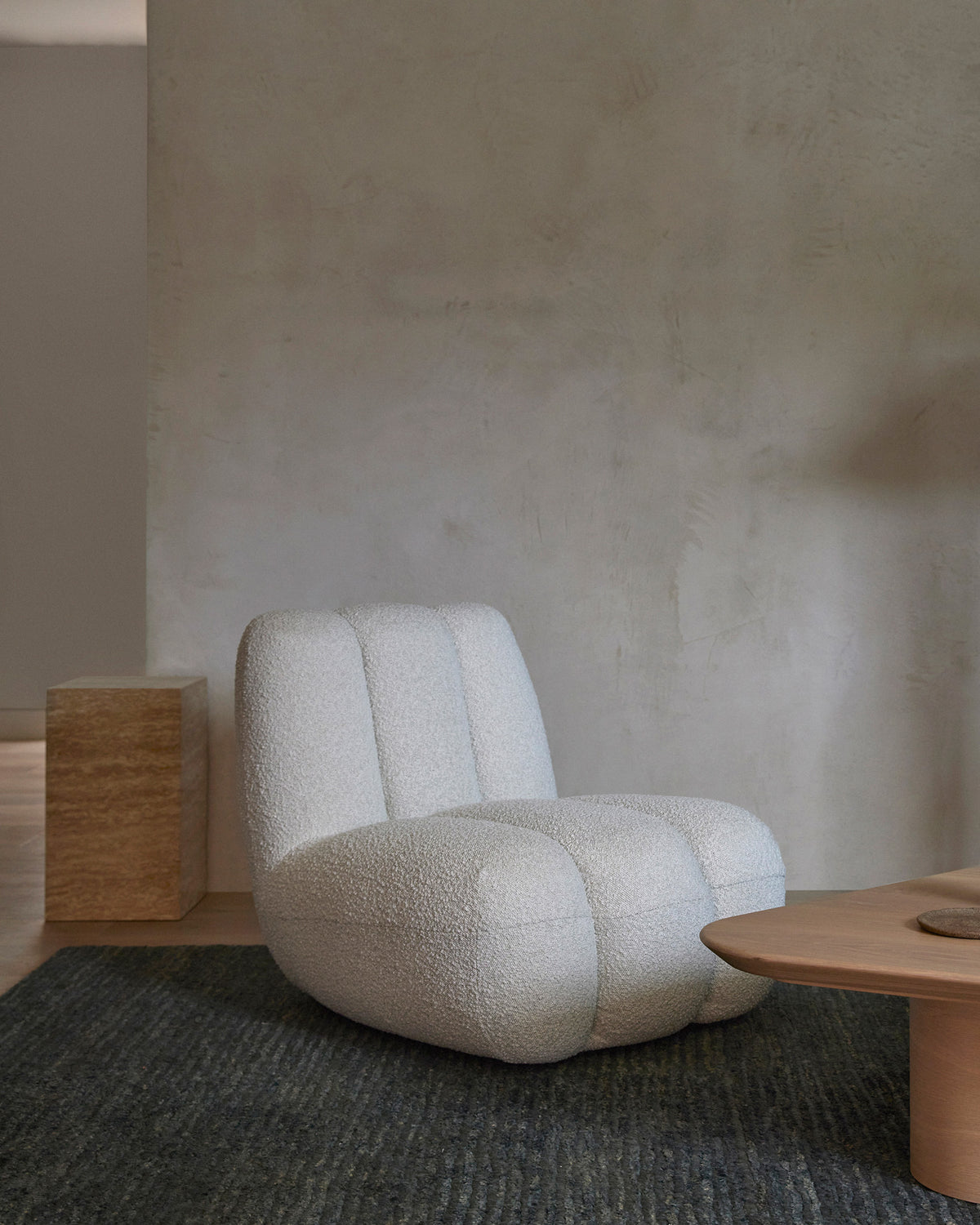 small cream travertine plinth side table next to a lounge chair